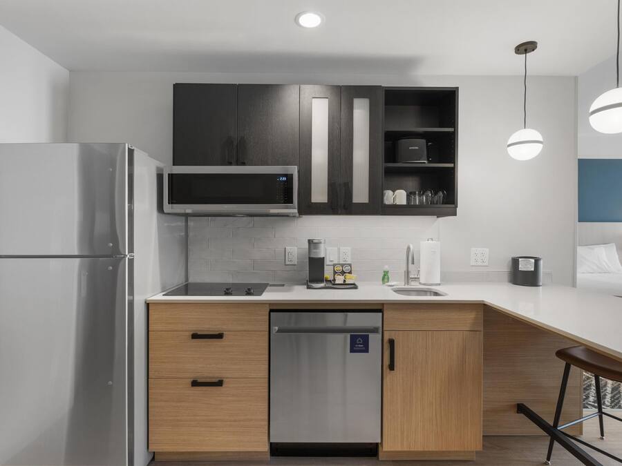 A modern kitchen with a stainless steel refrigerator, a microwave, and a coffee maker. There is a dishwasher and a bar stool.
