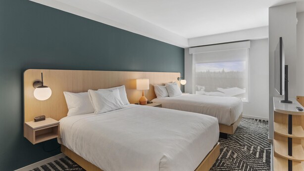 A hotel room with two beds, a TV, and a window with blinds.