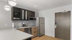 A modern kitchen with a stainless steel refrigerator, a microwave, and a dishwasher. There is a wooden countertop and a dark wooden door.