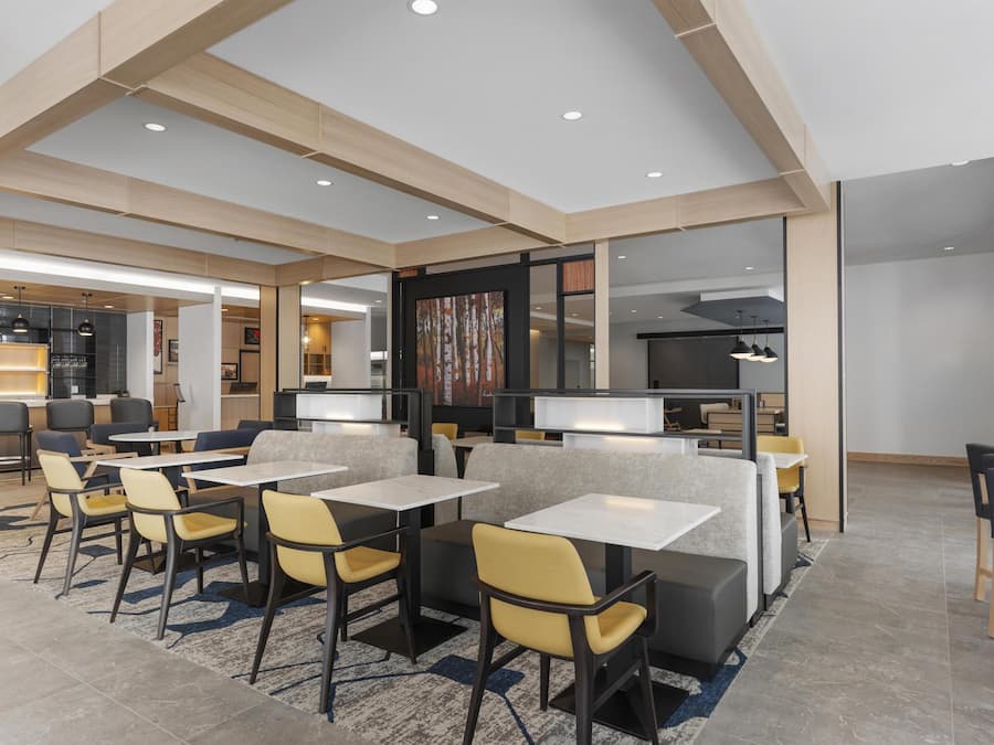 Un comedor moderno con techos altos, iluminación empotrada y una variedad de opciones de asientos, incluyendo mesas y cabinas.