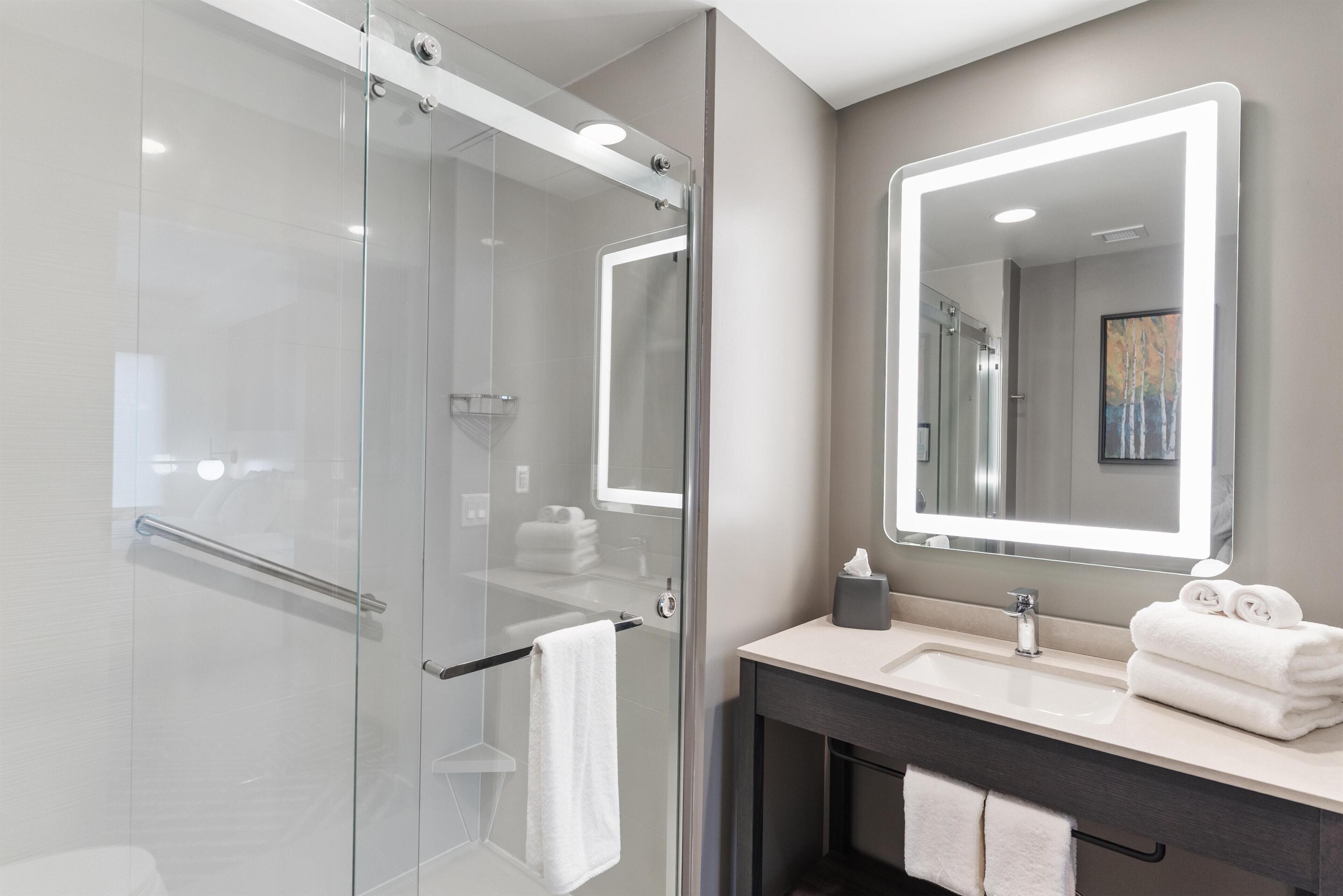 Un baño moderno con ducha vidriada, un espejo grande y un tocador con lavabo y toallero.