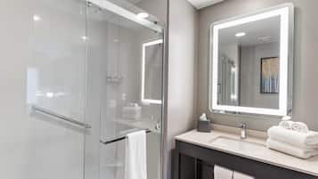 Un baño moderno con ducha vidriada, un espejo grande y un tocador con lavabo y toallero.