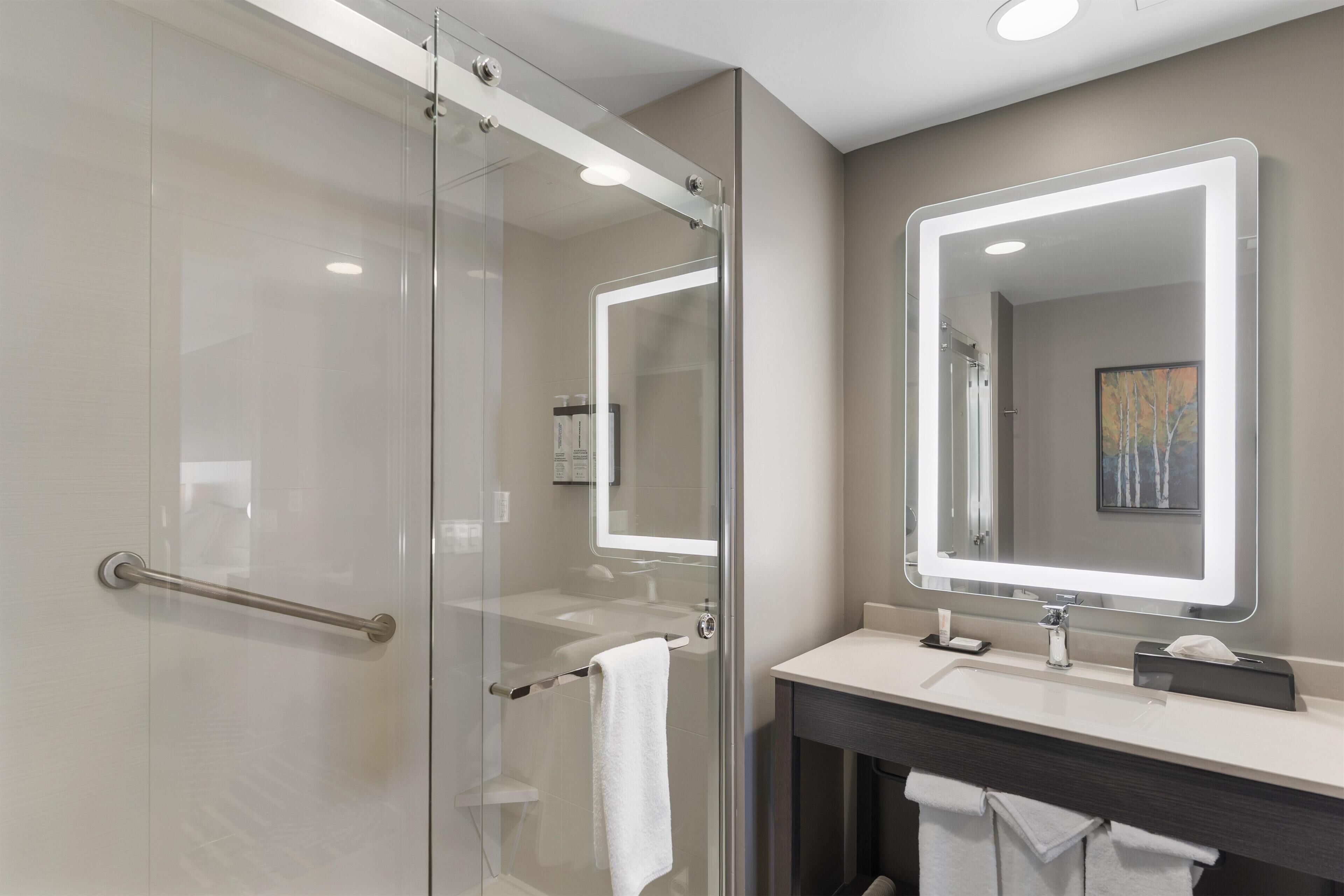 Une salle de bain moderne avec une douche à parois de verre, un meuble-lavabo doté d’un grand miroir et un porte-serviettes.