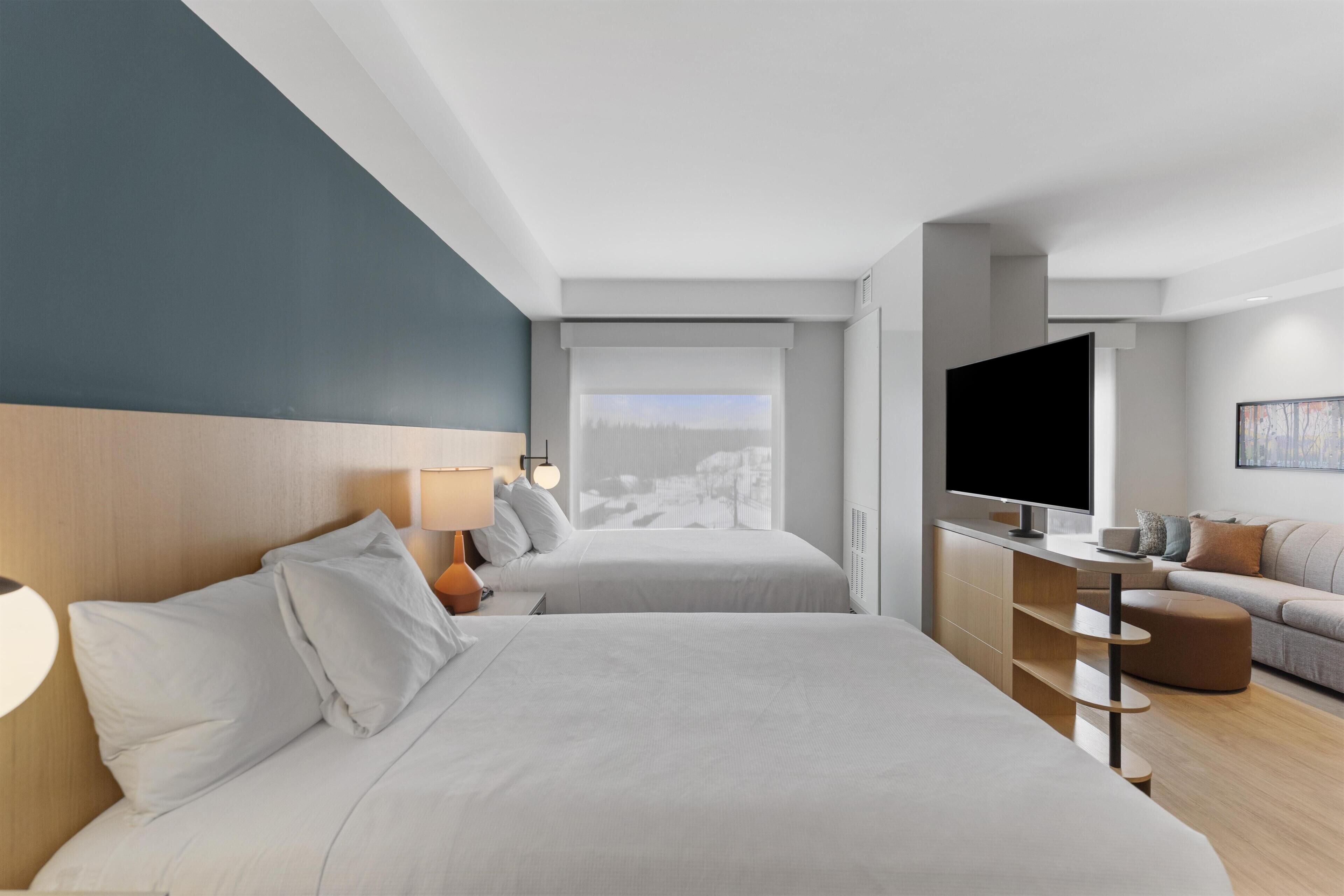 A hotel room with two beds, a TV, a sofa, and a view of a snowy landscape.