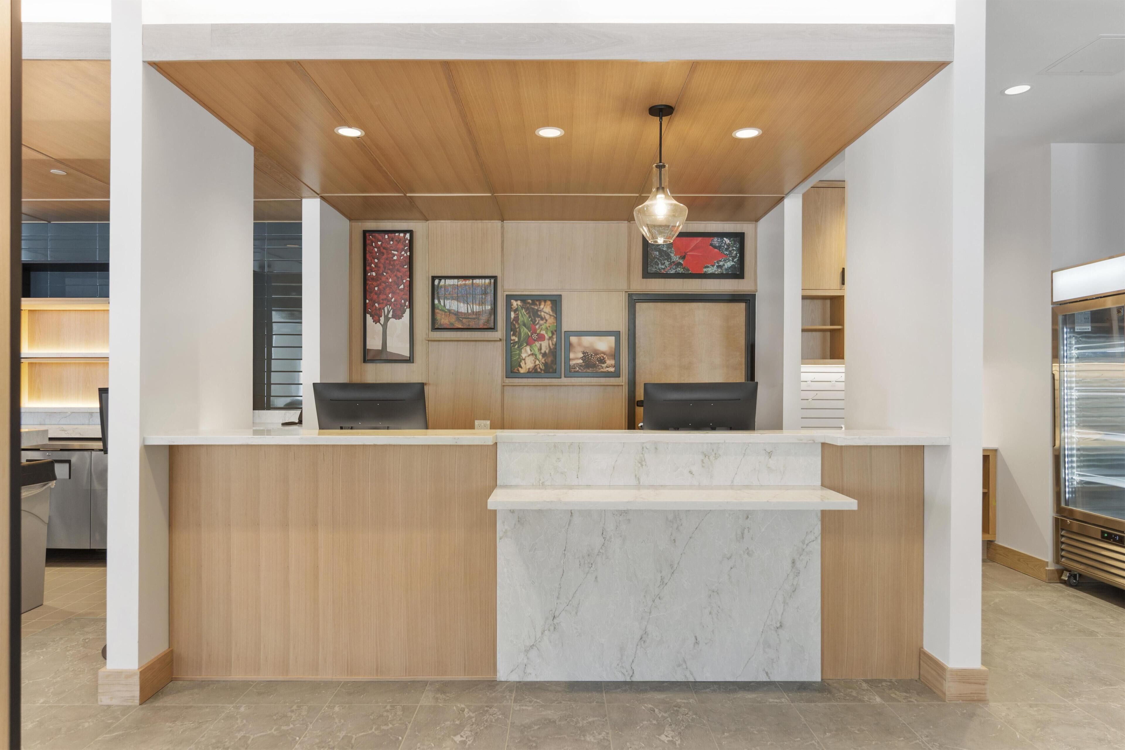A reception desk with a wooden finish, marble counter, and artwork on the wall.