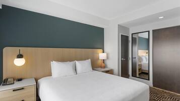 A hotel room with a large bed, bedside tables, a lamp, a phone, a mirror, and a wardrobe.