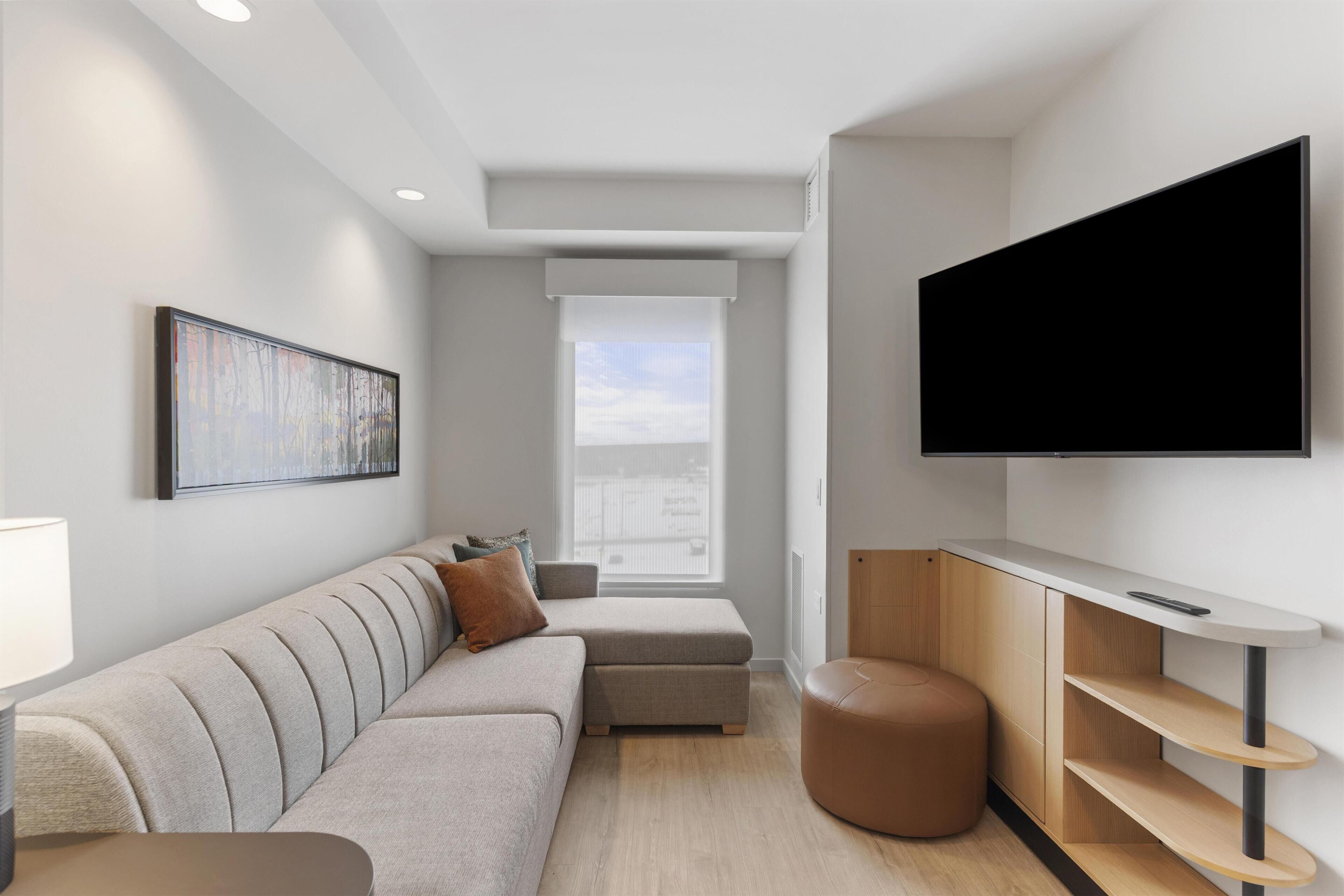 A modern living room with a sofa, ottoman, and a flat-screen TV mounted on the wall.