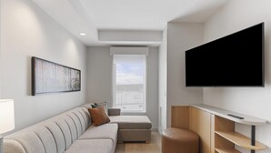 A modern living room with a sofa, ottoman, and a flat-screen TV mounted on the wall.