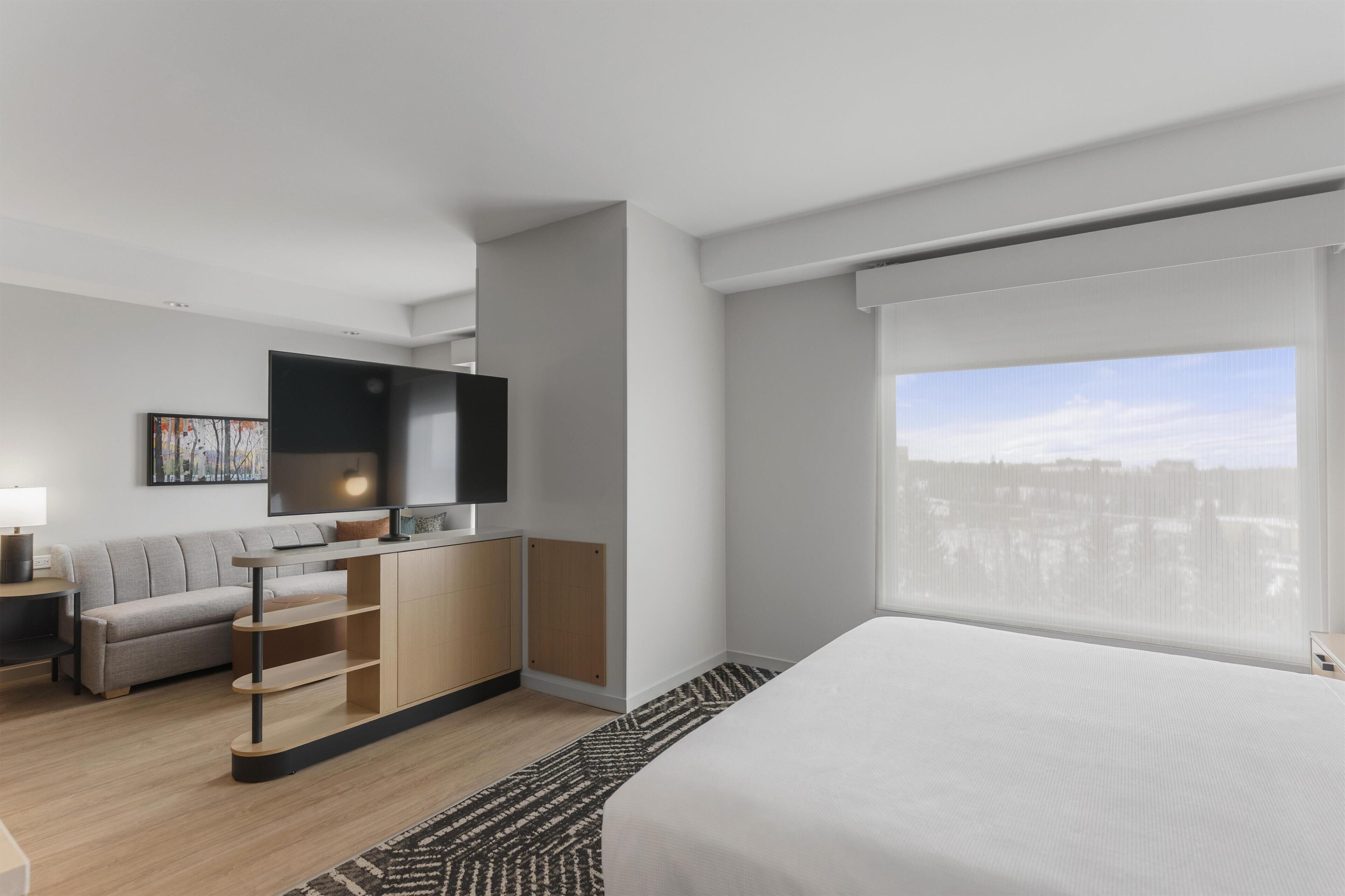 Una habitación de hotel moderna con cama, televisor, sofá y escritorio.