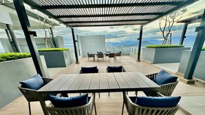 A covered outdoor seating area with a table and chairs, overlooking a cityscape. - Neu Suites Horizon View Apartments (Kuala Lumpur)