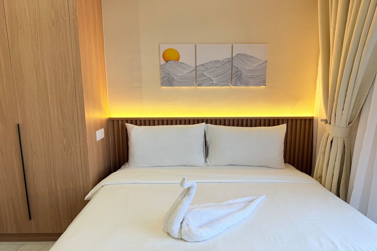 A hotel room with a bed, a wooden wardrobe, and a wall-mounted artwork depicting a sun and waves.