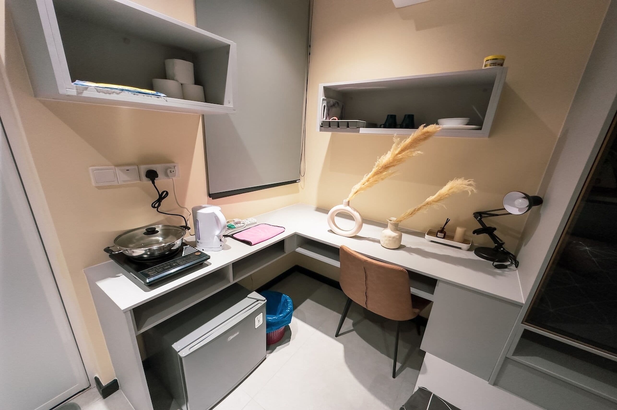 A compact kitchen with a stove, sink, and countertop. There are shelves above the counter holding kitchen items.