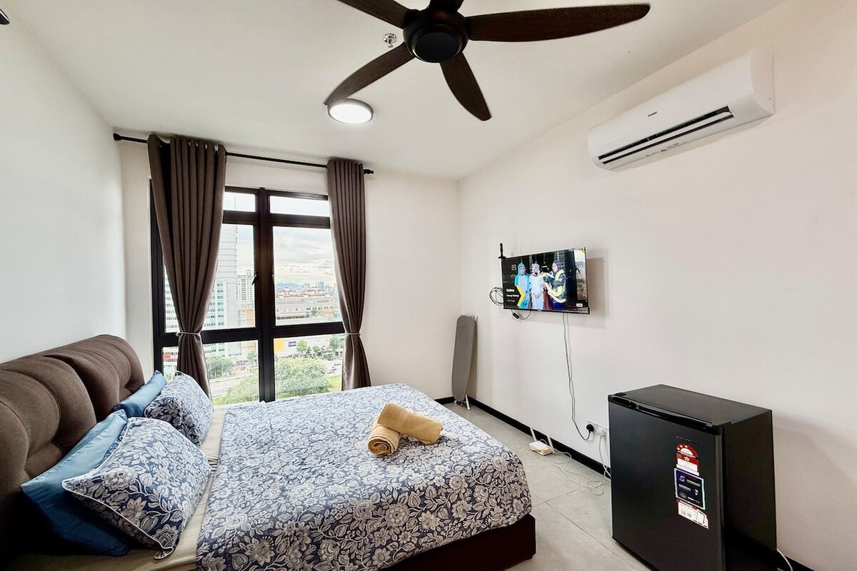 A hotel room with a bed, a ceiling fan, an air conditioner, a television, and a refrigerator.