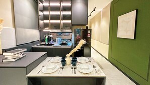 A modern kitchen with a built-in stove, a refrigerator, and a dining area set up with plates, cups, and cutlery. - Neu Suites Horizon View Apartments (Kuala Lumpur)