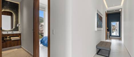 A modern hallway with a wooden door leading to a bathroom, a bench, and a view of the outside.