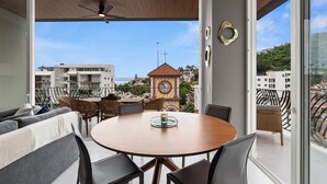 Een modern balkon met een ronde tafel en stoelen, een klokkentoren op de achtergrond en een helder uitzicht over de stad.
