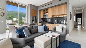 Een moderne woonkamer met een grijze bank, een salontafel en uitzicht op de stad en bergen door grote ramen.