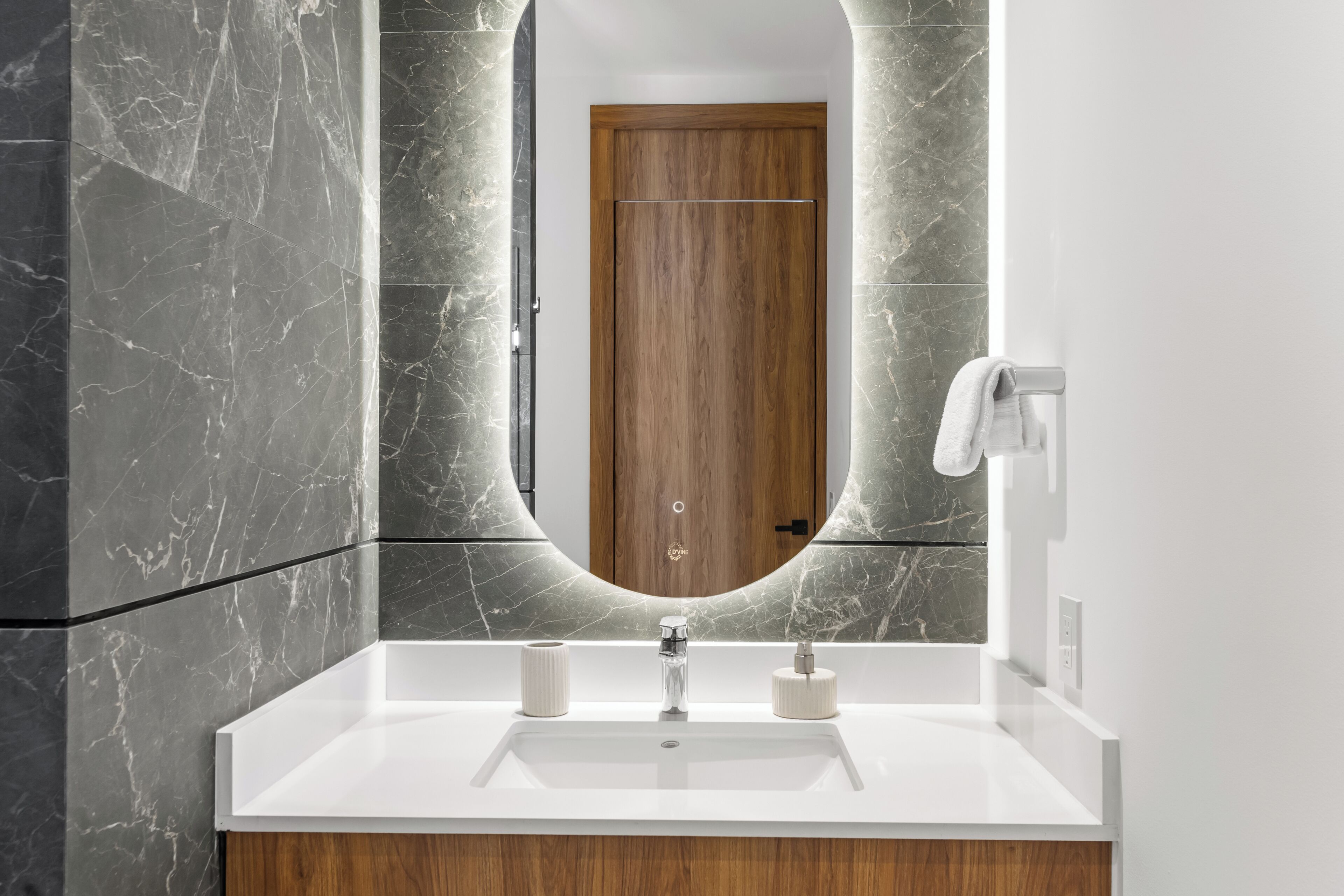 Un baño moderno con detalles de mármol, un lavamanos blanco y una puerta de madera.