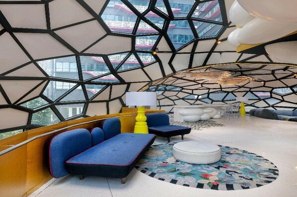 Un interior moderno con patrones geométricos en las paredes, un conjunto de sofá azul, un reposapiés redondo y una lámpara amarilla.