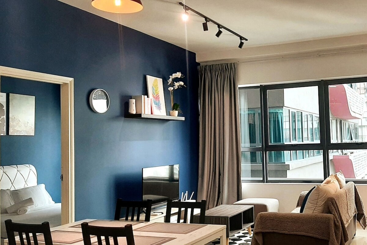 A modern living room with a blue accent wall, a dining area, and a large window with a view of buildings.