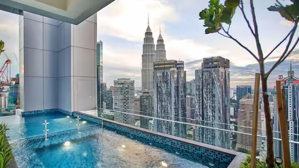 A modern indoor pool with a cityscape view, including the Petronas Towers, and a glass railing. - Royce Residence KLCC Skyview Apartments (Kuala Lumpur)