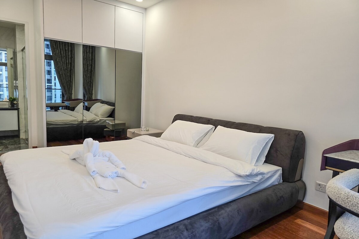 A modern hotel room with a large bed, a bedside table, a chair, and a mirror.