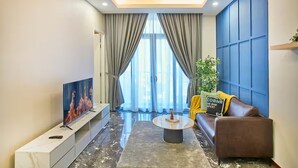 A modern living room with a flat-screen TV, a round coffee table, a sofa, and a large window with curtains. - Royce Residence KLCC Skyview Apartments (Kuala Lumpur)