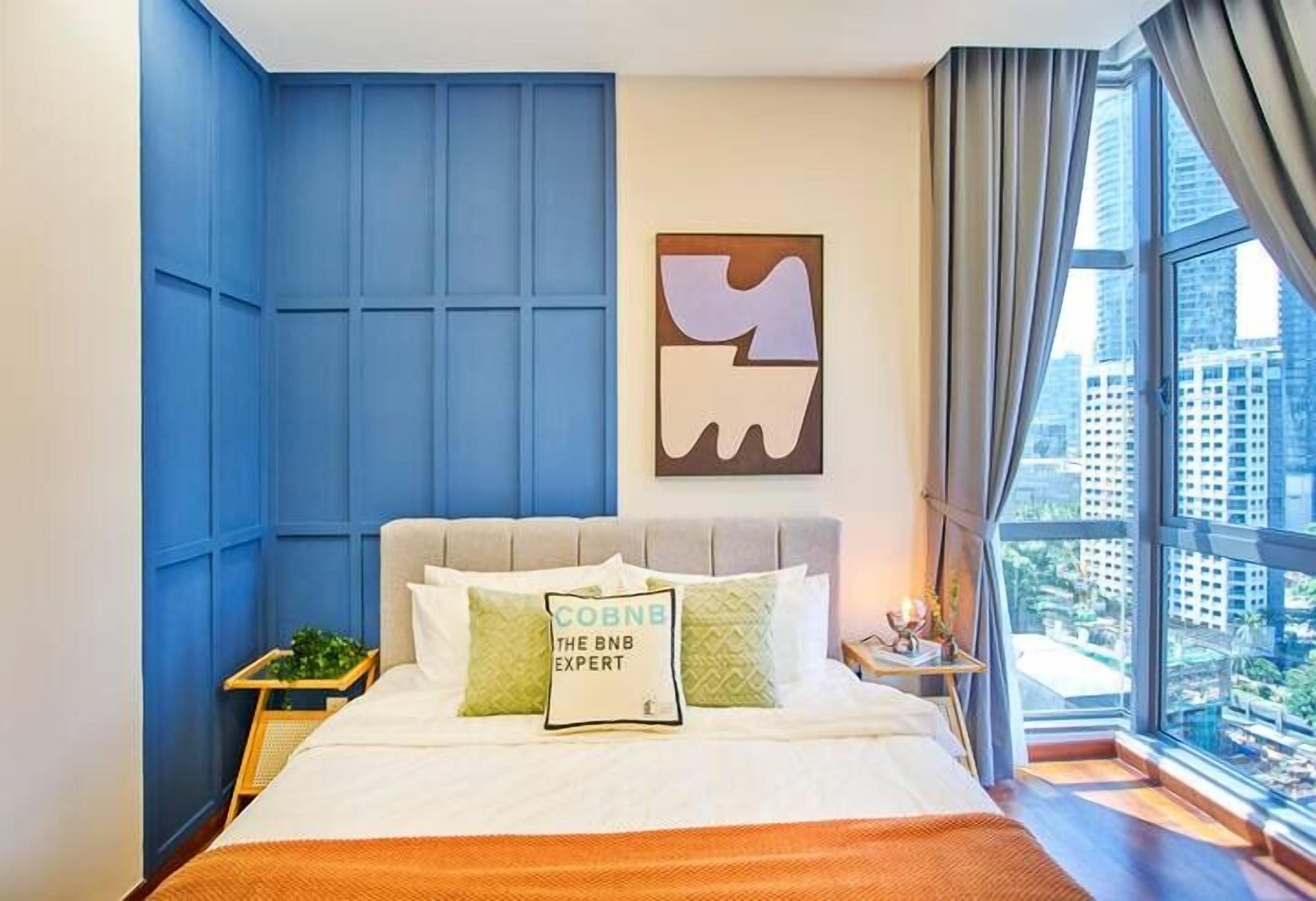 A modern hotel room with a large bed, a city view, and a blue accent wall.