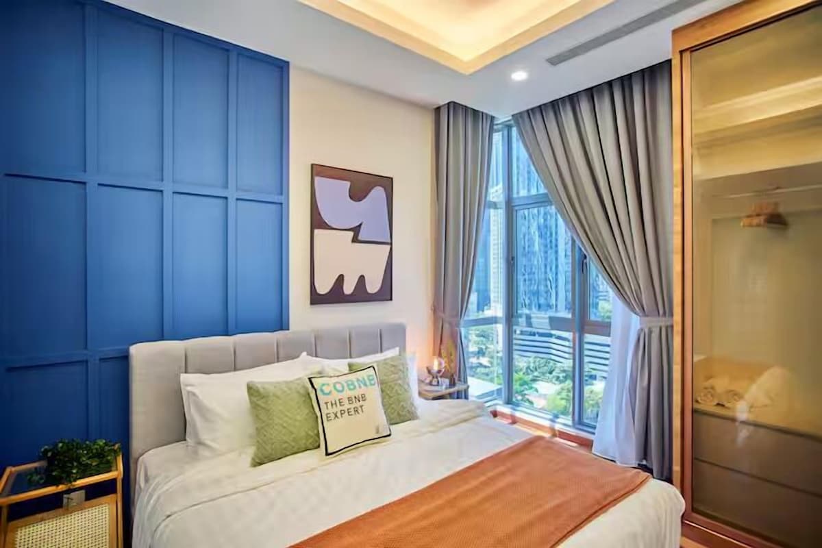 A modern bedroom with a large bed, a view of greenery outside, and a blue accent wall.