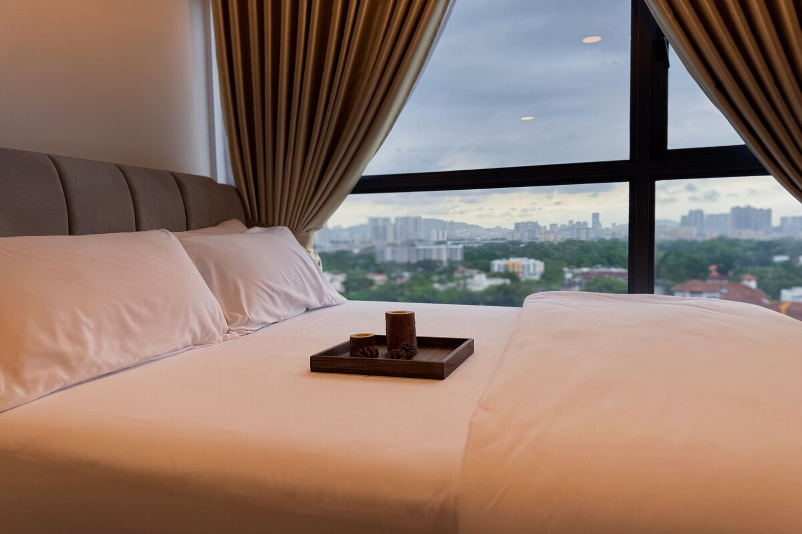 A hotel room with a large bed, a tray with candles, and a city view through the window.