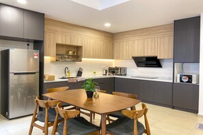 A modern kitchen with grey cabinets, a stainless steel refrigerator, a microwave, and a dining area with a wooden table and chairs. - The Reizz Residence by Emily in Town (Kuala Lumpur)