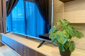 Un téléviseur à écran plat posé sur un meuble télé en bois, avec un pot contenant une plante monstera à côté.