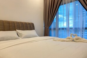 Une chambre d’hôtel avec un grand lit, du linge de lit blanc et une vue sur le paysage urbain à travers des rideaux transparents.