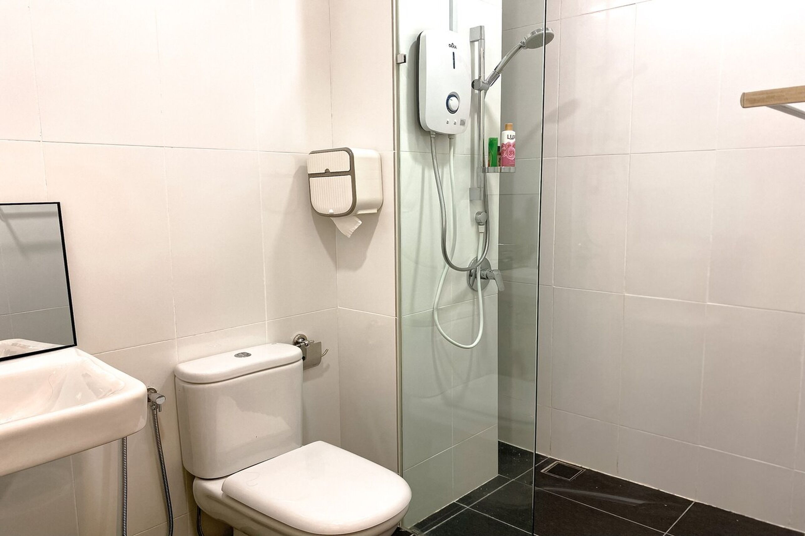 Egy modern fürőszoba, amelyben található egy WC, egy üvegfalas zuhanyzó és egy kézszárító.