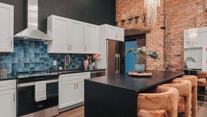 A modern kitchen with white cabinets, a black countertop, and a brick wall. - Starr Piano: Roxie Suite –  Walk to Broadway! (Nashville)