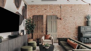 A cozy living room with a brick wall, a flat-screen TV, a piano, and comfortable seating. - The Carraway Suite • Luxury • Walk to Broadway! (Nashville)