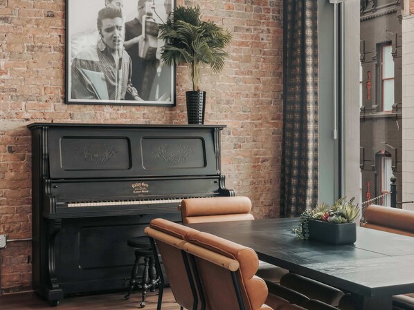 A room with a black piano, leather chairs, a table, and a framed picture on the wall.