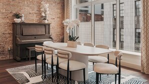 Un comedor con una mesa grande, seis sillas, un piano y un ventanal con vistas a un edificio.