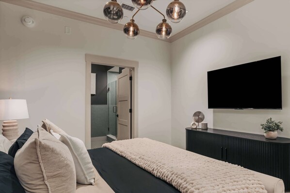 A modern bedroom with a bed, bedside table, lamp, and a flat-screen TV mounted on the wall.