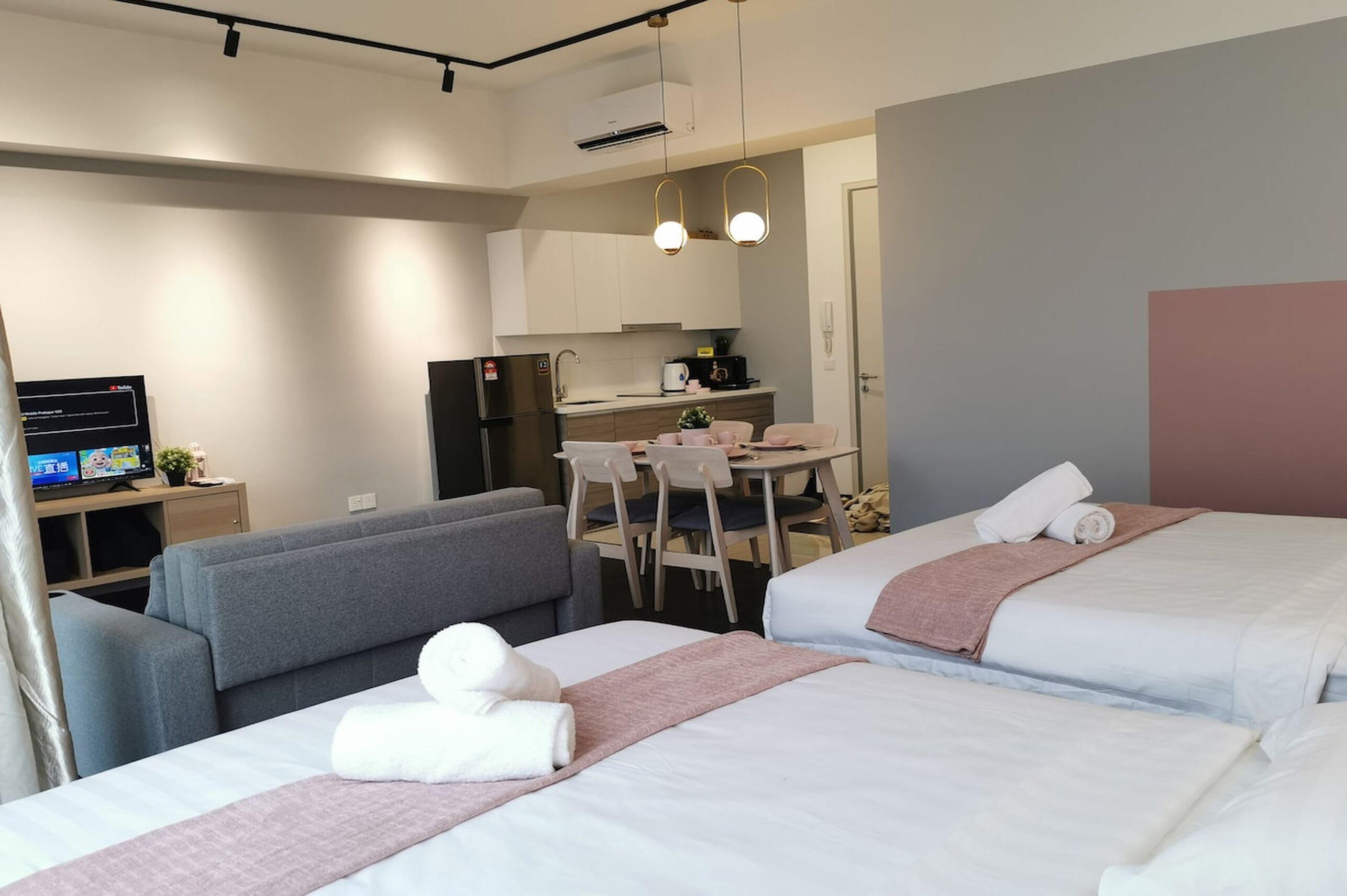 A hotel room with two beds, a sofa, a desk with a computer, and a kitchenette.