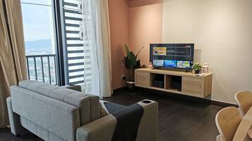 Una sala de estar moderna con un sofá gris, un mueble de televisión de madera y vistas a la ciudad a través de ventanas amplias.