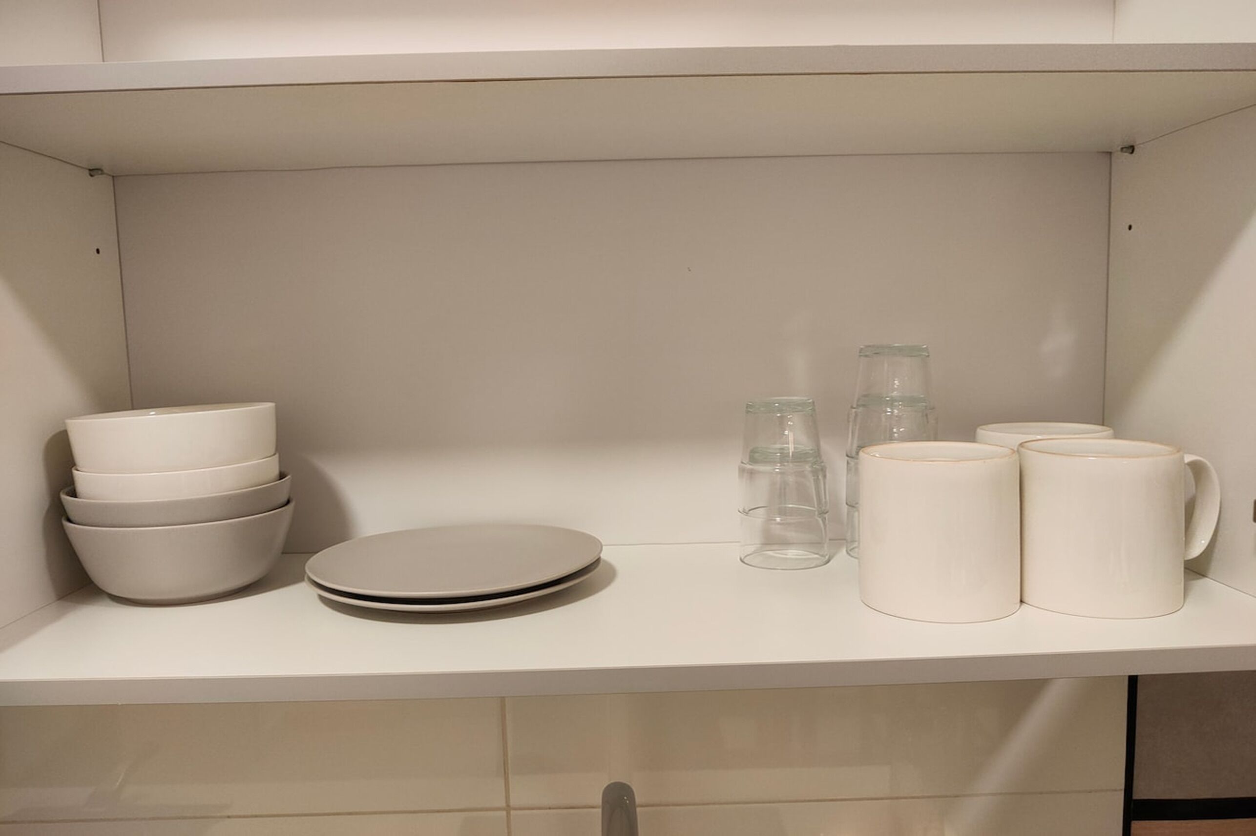 A kitchen with white cabinets, a stack of bowls, plates, and clear glass mugs.