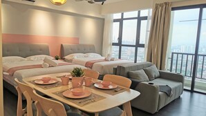A hotel room with three beds, a dining table set with pink tableware, a sofa, and a large window offering a city view. - 28 Boulevard Residence KLCC Skyview (Ampang)