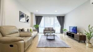 Un salon moderne avec un canapé beige, un canapé plus petit, une table basse et un téléviseur posé sur un meuble en bois.