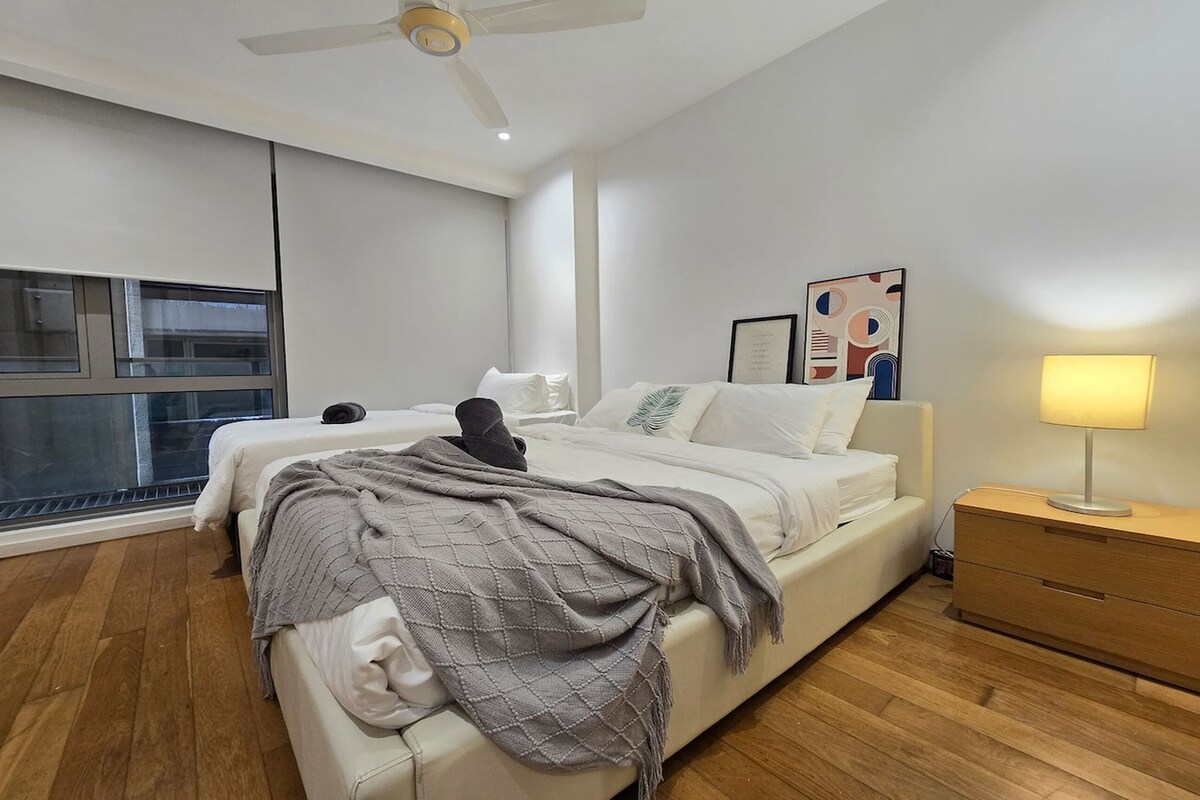 A modern bedroom with a bed, a nightstand, a lamp, and a window.
