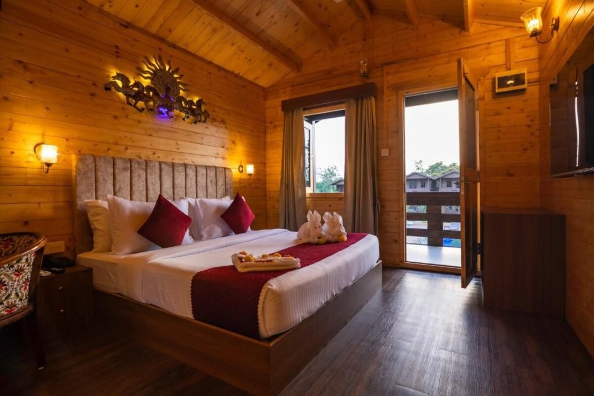 A wooden room with a bed, two wall-mounted lights, a decorative wall piece, and a door leading outside.