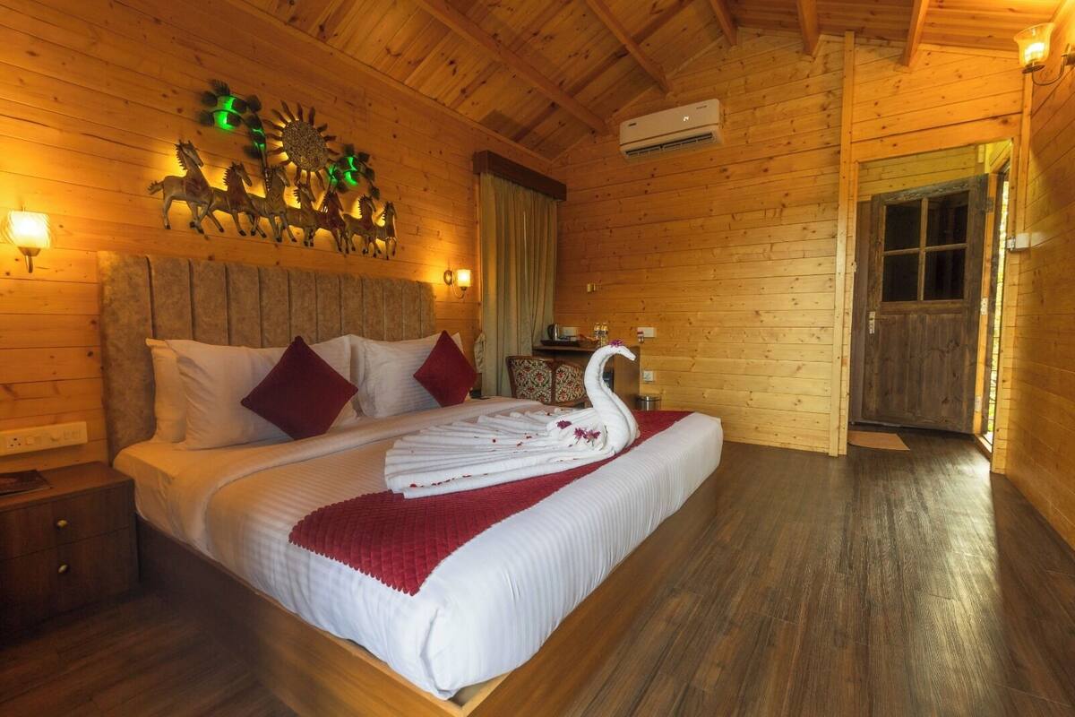 A wooden cabin-style bedroom with a bed, pillows, a wall-mounted clock, and a swan-shaped towel arrangement.