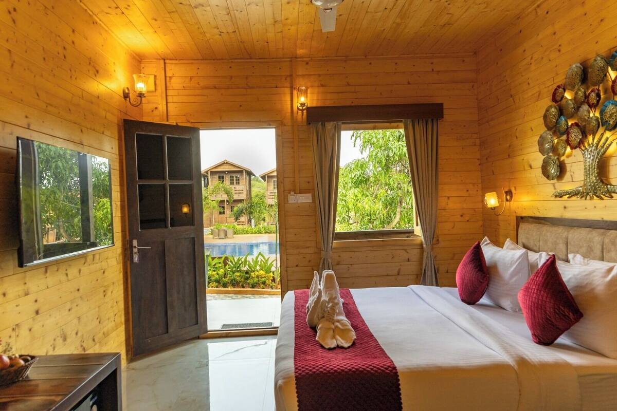 A wooden room with a bed, a window, and a view of a pool and buildings outside.