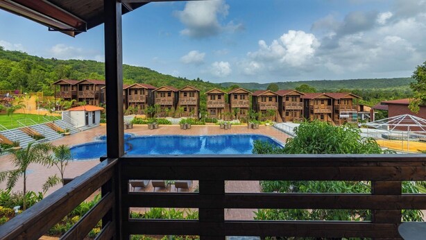 A resort with multiple wooden cabins, a swimming pool, and a view of green hills.