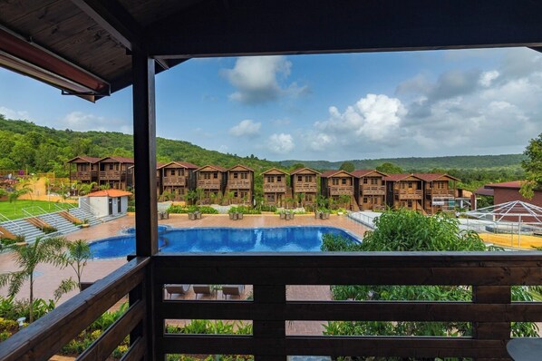 A resort with multiple wooden cabins, a swimming pool, and a view of green hills.